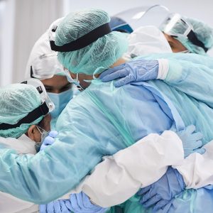 Medical professionals embracing each other in ICU. Doctors and nurses are in protective coveralls after successful treatment. They are at hospital during COVID-19.
